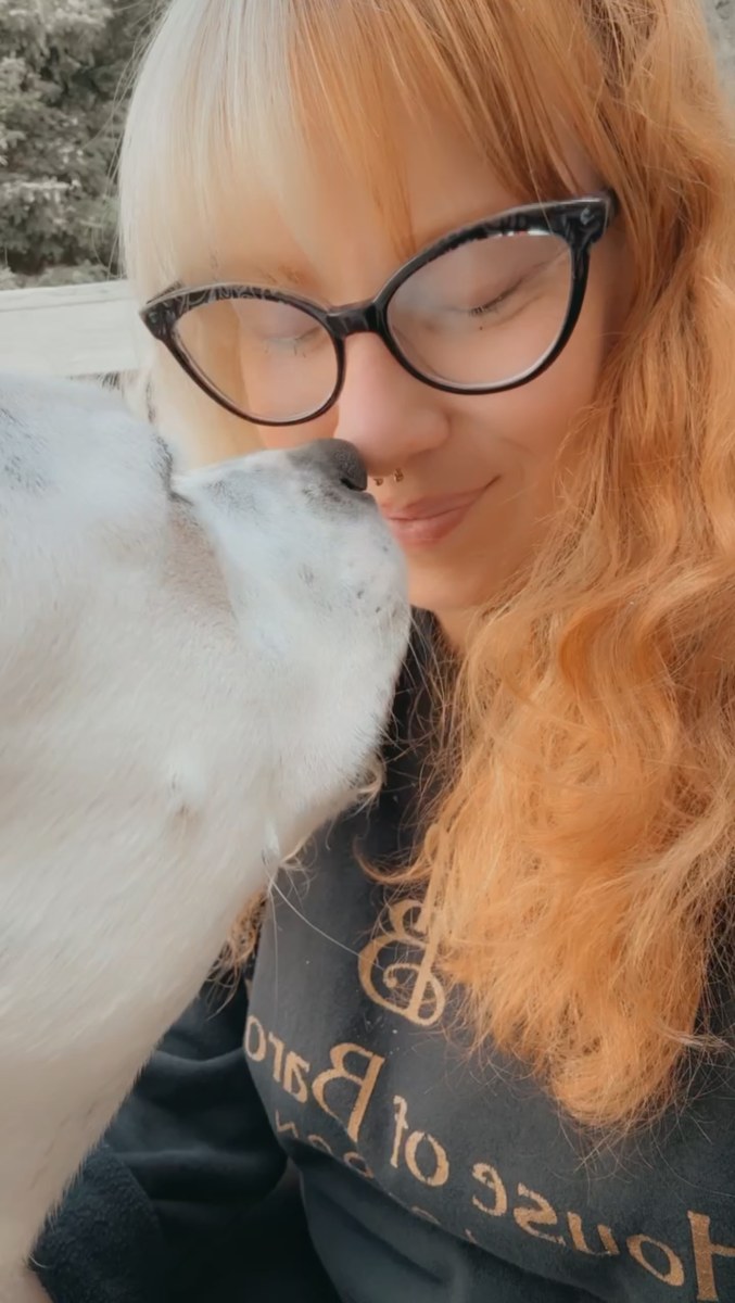 Red Morris receiving an affectionate kiss from a white dog